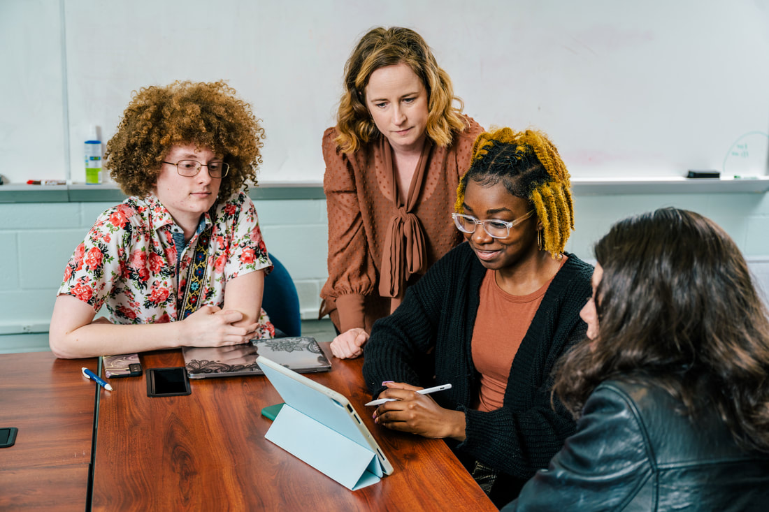 Dr. Jensen leaning in as three students review work on a tablet