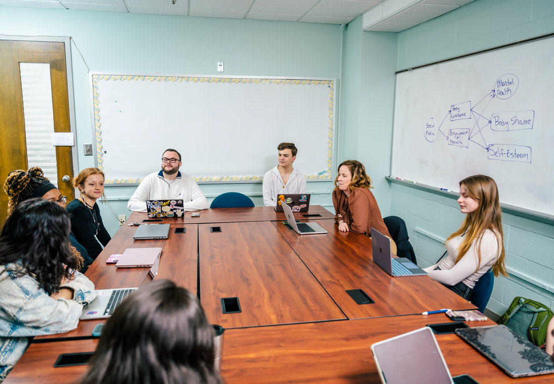 Dr. Jensen and students around a conference table, with a whiteboard diagram linking social media to body image, self-esteem and mental health